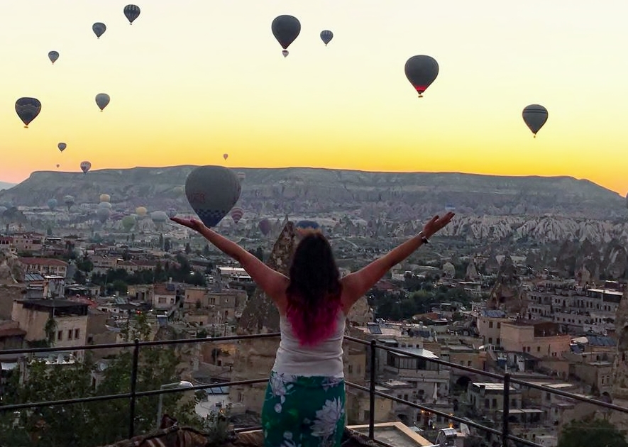 How To Change Your Life . A picture of a girl standing on a rooftop in Cappadocia [Turkey] watching the hot air balloons,  in the early morning rising sun flying, across the ancient city's skyline.