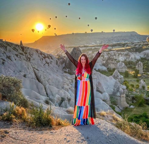 The Power Of Gratitude - Gratitude And Attitude Are Not Challenges, They Are Choices. Picture of a woman in a multi-coloured dress with her arms in the air saluting the rising sun.